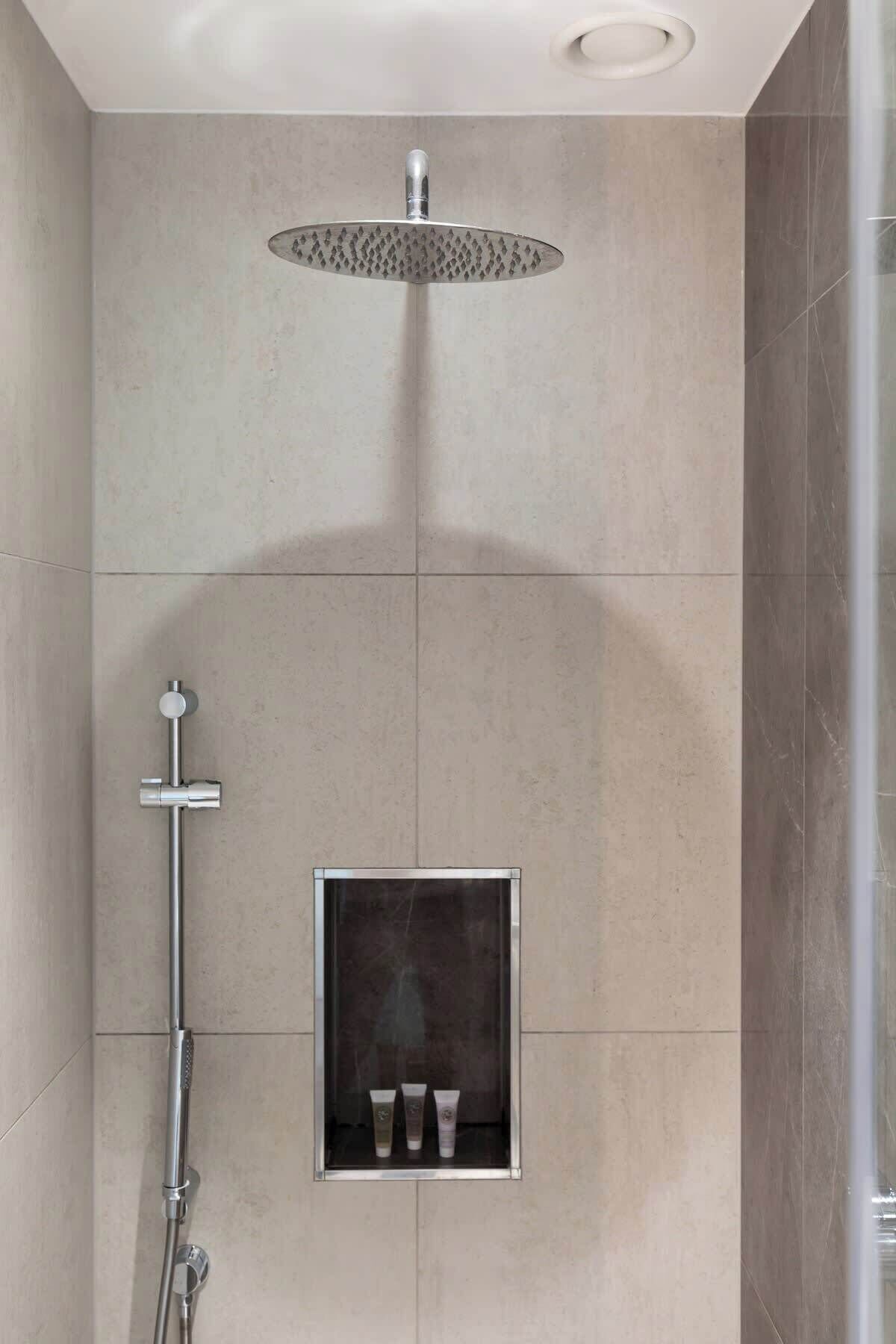 A modern shower with a rain showerhead, a handheld showerhead, and a built-in shelf with toiletries.