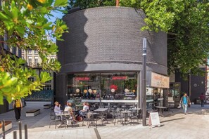 Ein Straßencafé mit Tischen und Stühlen, einer Ziegelwand und Schildern für eine Cocktailbar und ein Espressohaus.