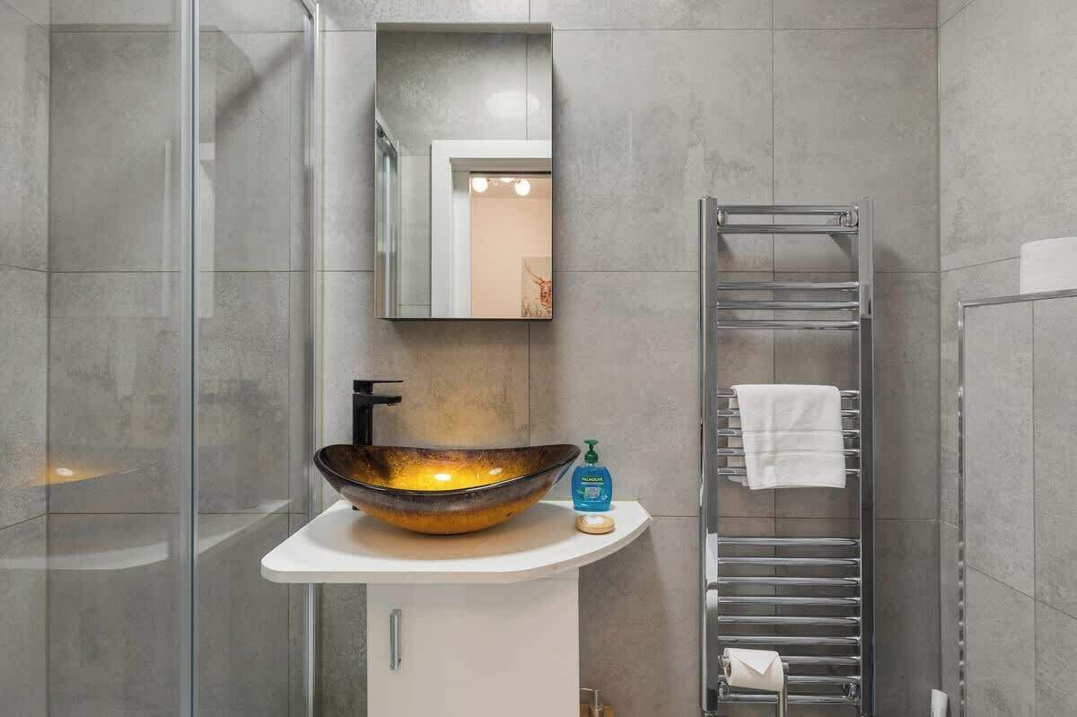 Een moderne badkamer met een glazen douchecabine, een wastafel op voet, een handdoekrek en een spiegel.