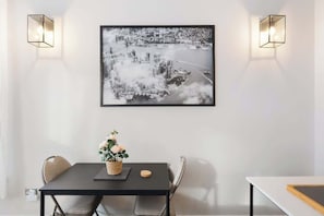 A dining area with a table, chairs, a framed cityscape photograph, and wall-mounted lights. - Stunning 2BR/2BA-ClaphamCommon (Greater London)