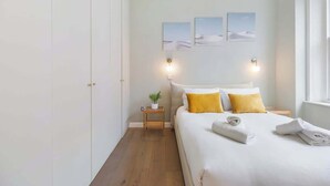 Ein Schlafzimmer mit einem Bett, zwei Nachttischen, einer Stehlampe, einer Zimmerpflanze und Wandleuchten.