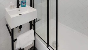 Ein modernes Badezimmer mit Duschkabine aus Glas, Waschbecken in Weiß und Spiegel sowie Toilettenartikeln.