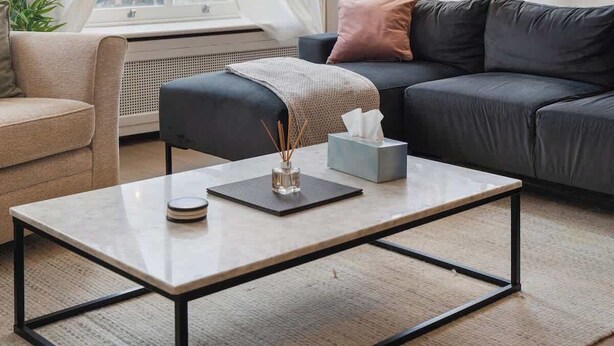 Ein Wohnzimmer mit einer Couch, einem Couchtisch, einer Lampe und Blick ins Freie durch große Fenster.