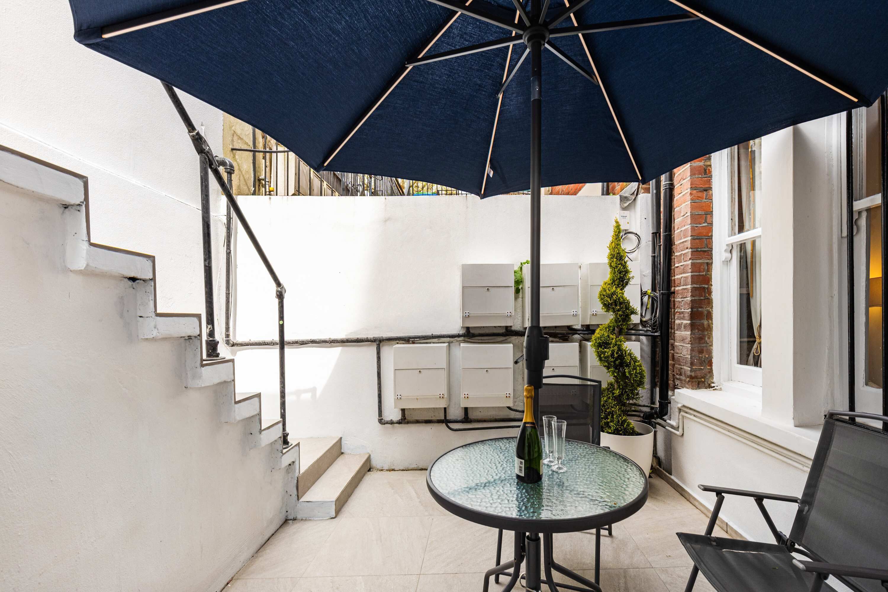 Une table en verre, un parasol bleu, une plante en pot et une bouteille de champagne.