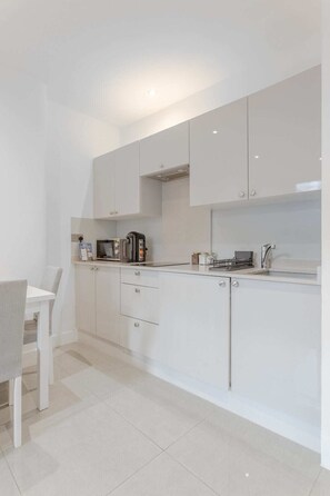 A modern kitchen with white cabinetry, a built-in microwave, and a stainless steel sink. - Modern 1 BR w/AC - Paddington (Greater London)