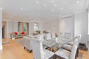 A modern dining area with a glass table and chairs, a sofa with red cushions, and a window with curtains. - Luxury 5 Bedroom & 4 Bathroom - Garden,Cinema,Gym (Greater London)