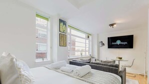 Et moderne hotelværelse med en seng, to siddepladser, et fladskærms-tv og et vindue med skodder.