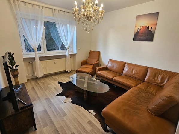 Un salon comprenant un canapé, un fauteuil, une table basse en verre et un lustre.