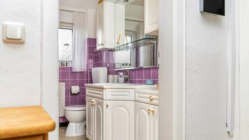 Een badkamer met toilet, wastafel, spiegel en paars betegelde wanden.