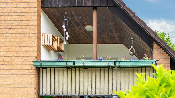 Un balcón con baranda de madera, una lámpara colgante y un toldo verde adornado con flores.