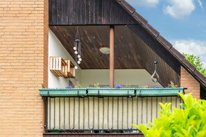 A balcony with a wooden railing, a hanging light fixture, and a green awning with flowers. - Apartment 'Otter' with Balcony and Wi-Fi (Lachendorf)