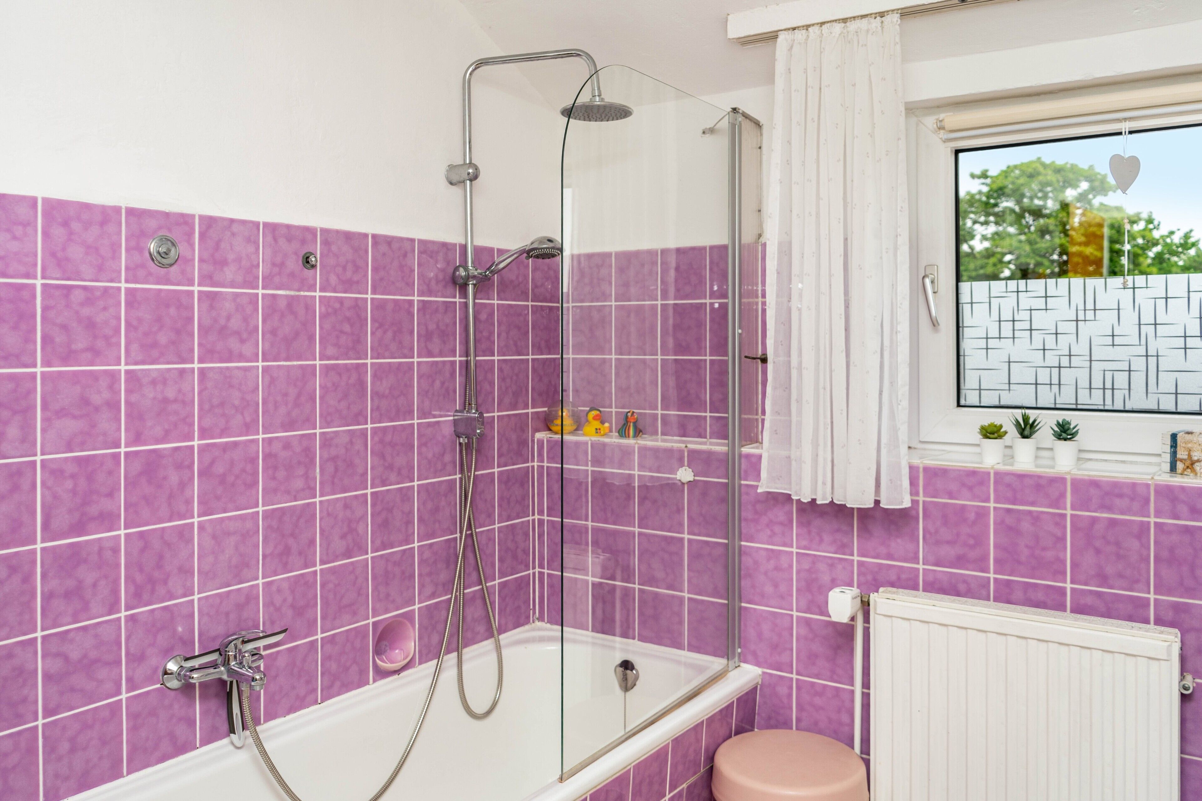A bathroom with a glass-enclosed shower, a white bathtub, and a window with a view of trees.