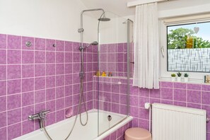 A bathroom with a glass-enclosed shower, a white bathtub, and a window with a view of trees. - Apartment 'Otter' with Balcony and Wi-Fi (Lachendorf)