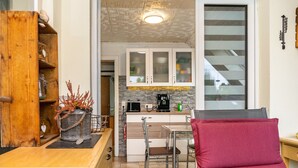 Cocina compacta con zona de comedor, que incluye un armario de madera, una silla de metal y un cojín rojo.