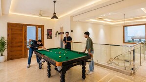 Une table de billard dans une pièce bien éclairée, avec un escalier et une vue sur un bâtiment à l’extérieur.
