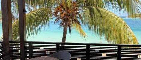 A covered outdoor seating area with a view of a beach and palm trees.
