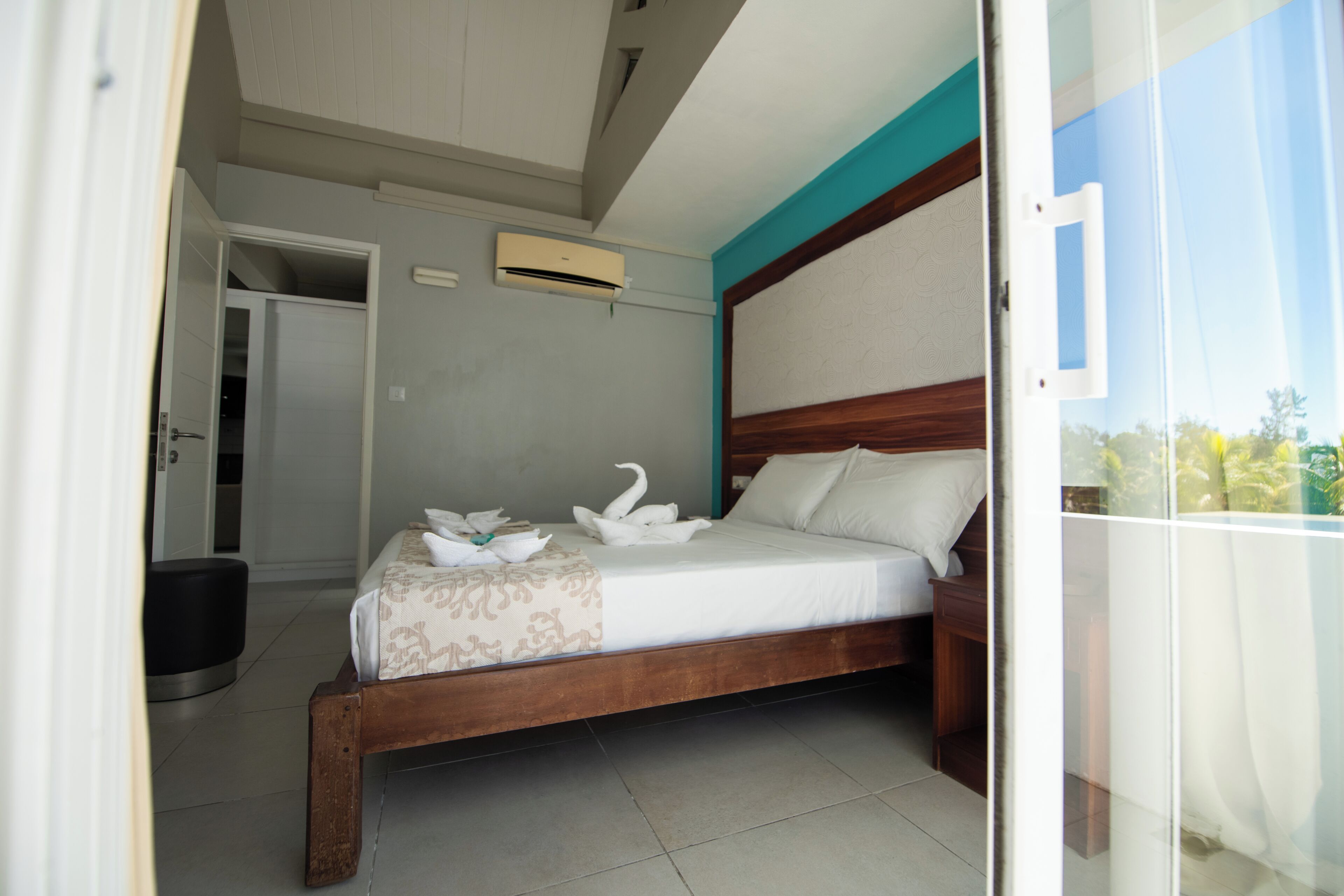 A bedroom with a wooden bed, a bedside table, a wall-mounted air conditioner, and a door leading to another room.