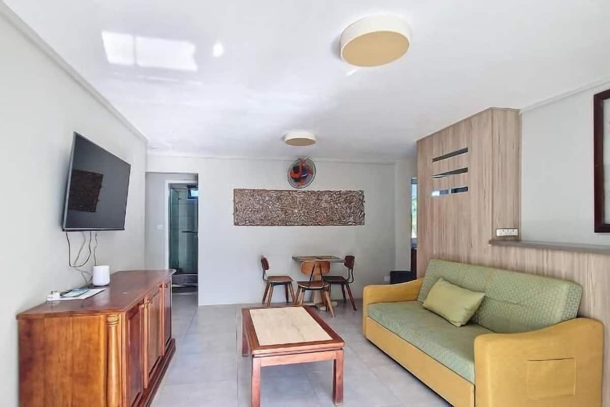 Un salon moderne comprenant un meuble en bois, un téléviseur, un canapé, une table basse et un coin repas avec des chaises.