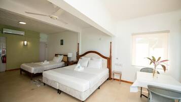 A hotel room with two single beds, a wooden headboard, a small table with a chair, and a window with a plant.