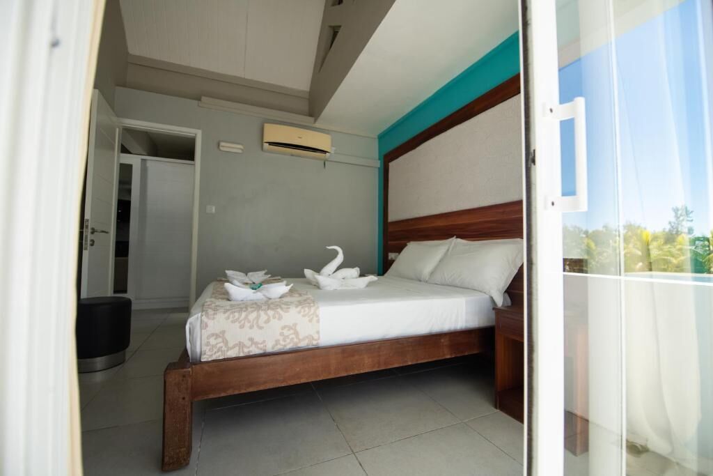 Un dormitorio con cama de madera, una mesita de noche, aire acondicionado instalado en la pared y una puerta que da a otra habitación.