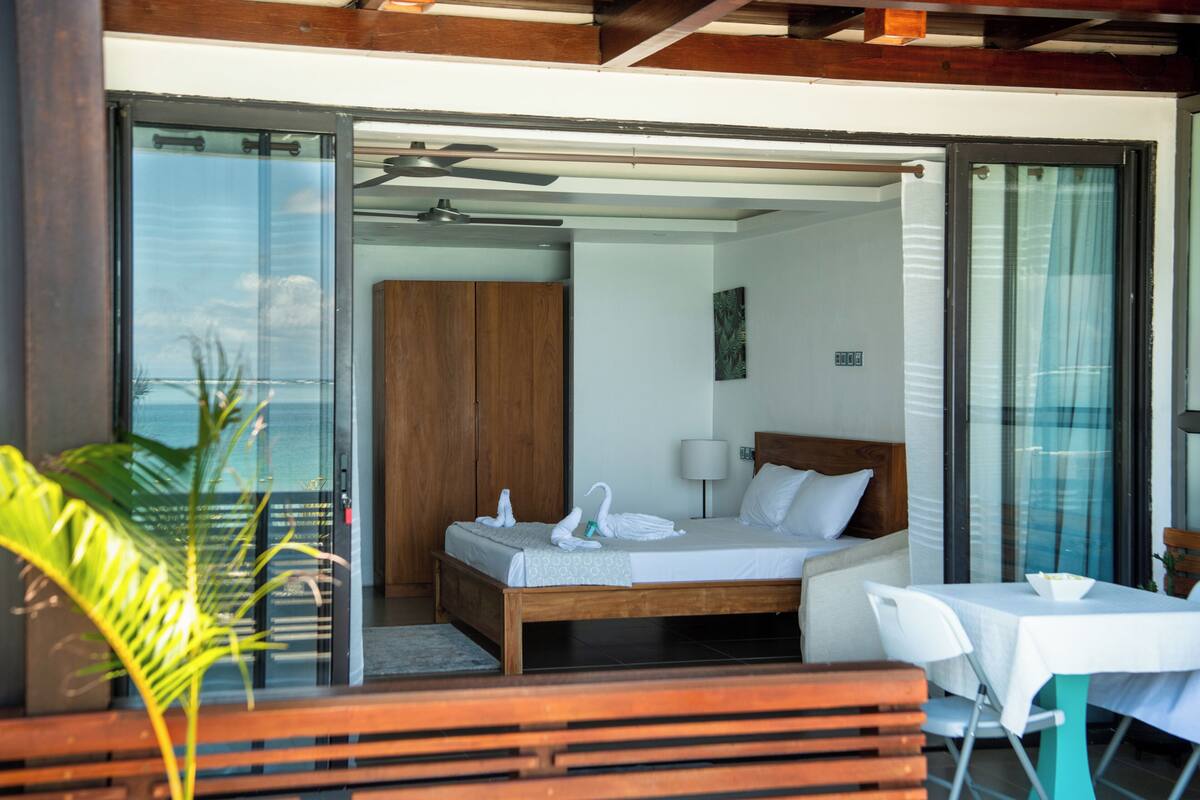Une chambre à coucher avec un lit, une table de chevet, une lampe et une vue sur l’extérieur, visible à travers une porte vitrée.