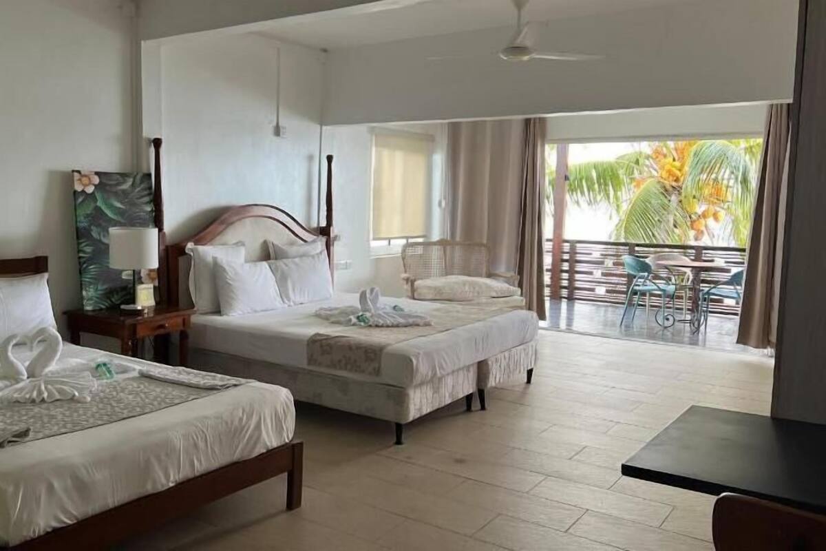 Une chambre d’hôtel avec deux lits, un balcon doté d’un espace salon extérieur et une vue sur les palmiers.