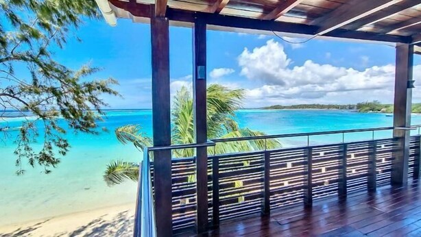 Een houten terras met uitzicht op een turquoise oceaan en palmbomen.