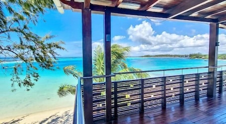 A wooden deck with a view of a turquoise ocean and palm trees.