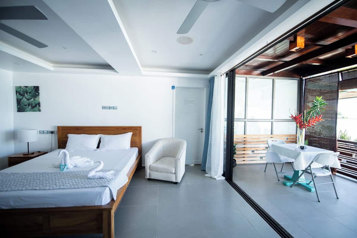 Une chambre d’hôtel moderne dotée d’un grand lit, d’un coin salon avec une table et des chaises, et offrant une vue à travers une porte vitrée.