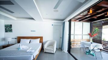 Habitación de hotel moderna con una cama grande, una zona de estar con una mesa y sillas, y vistas a través de una puerta de vidrio.