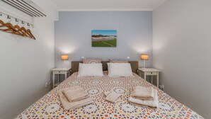 Un dormitorio con cama, dos mesitas de noche, un calentador de pared y un cuadro de un paisaje.