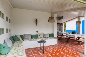 A covered patio area with a sofa, tables, and hanging lights. - Apartment 'Cottage 1' with Shared Pool, Wi-Fi and Air Conditioning (Alcácer do Sal)