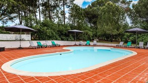 Una piscina con suelo de baldosas, rodeada de sillas de descanso y sombrillas.