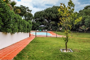 A swimming pool with a tiled deck, surrounded by a grassy area and trees. - Apartment 'Cottage 1' with Shared Pool, Wi-Fi and Air Conditioning (Alcácer do Sal)