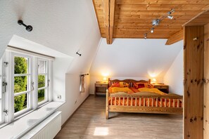 Et soveværelse med skråvæg, en træseng, et natbord med lampe og et vindue med udsigt over grønne områder.