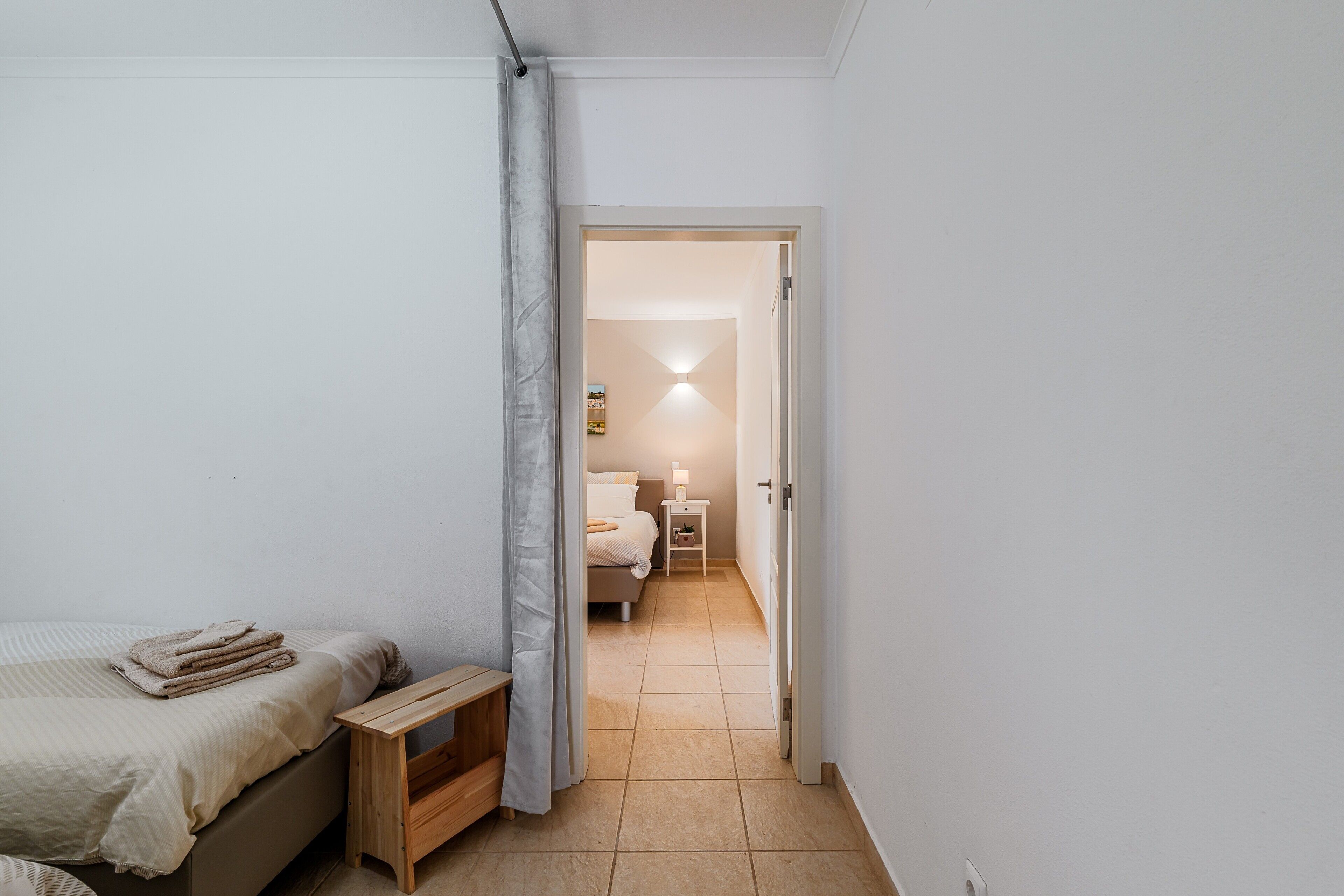Quarto com cama, mesa de cabeceira, abajur e porta para outro cômodo.