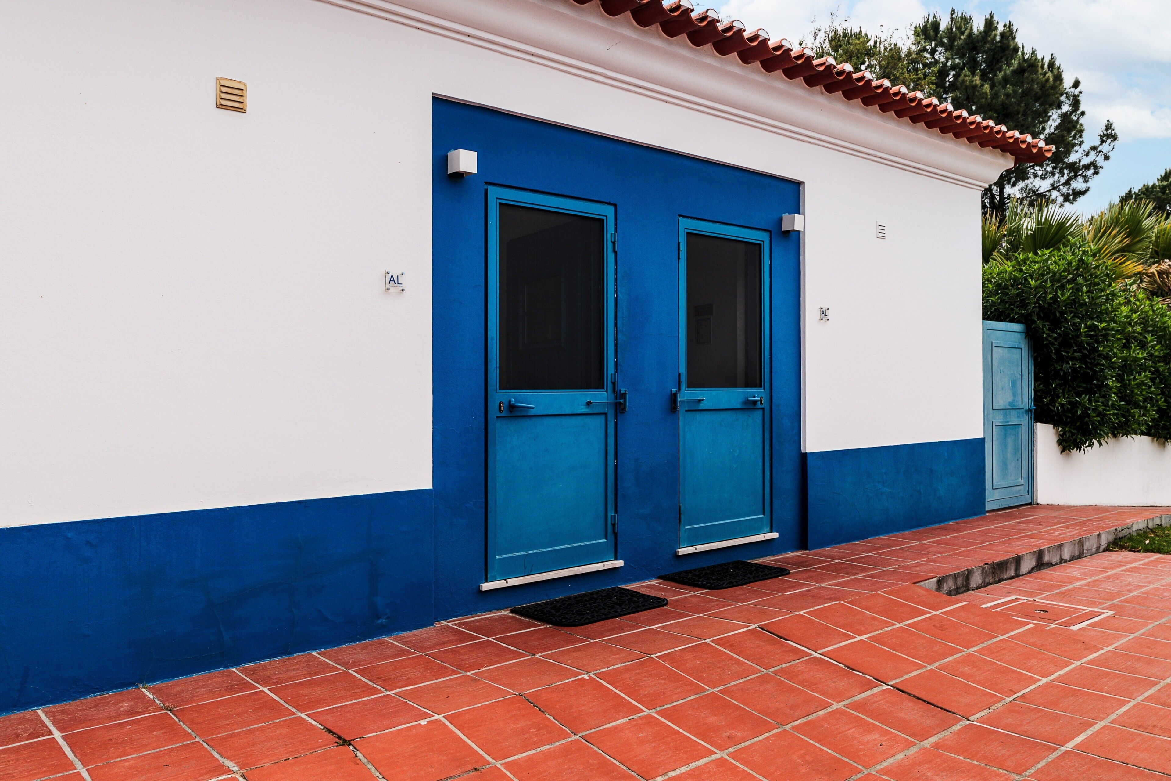 Un bâtiment avec deux portes bleues, une façade blanche et bleue, et un sol recouvert de carreaux rouges.
