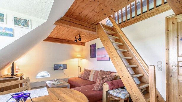 Une pièce de style loft avec un escalier en bois, un canapé, une table à manger et une lampe.