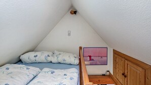 Une petite pièce triangulaire contenant un lit, un banc en bois et un tableau accroché au mur.