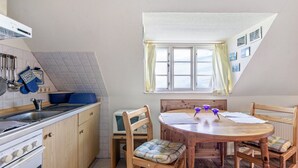 Une cuisine avec un coin repas, une fenêtre avec des rideaux et un plafond carrelé.