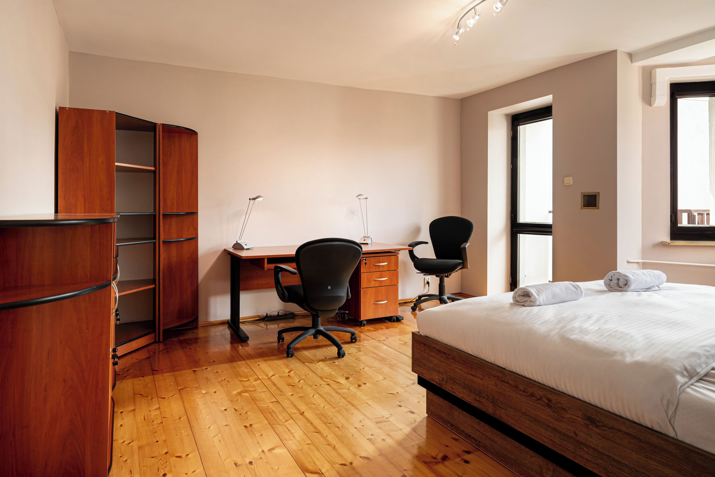 A bedroom with a wooden bed, a desk with a chair, a wardrobe, and a window.