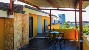 A covered outdoor area with a tiled floor, a table with chairs, and a view of buildings in the background. - Blue Nest Ottava (Sassari)