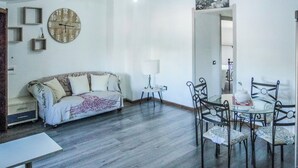 A living room with a sofa, a dining table with chairs, a wall clock, and a hanging light fixture. - Blue Nest Ottava (Sassari)