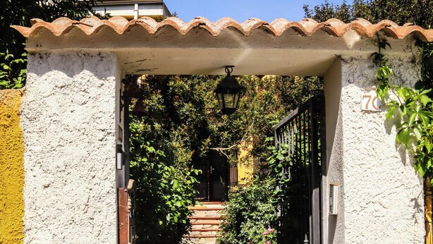 A narrow pathway leading to a building entrance with a tiled roof, surrounded by greenery. - Blue Nest Ottava (Sassari)
