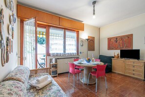 Um quarto com uma cama, uma mesa de jantar com cadeiras, uma televisão e uma janela com cortinas.