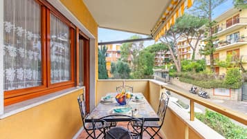 Varanda com mesa posta para refeições, uma cadeira e vista para a rua e edifícios.