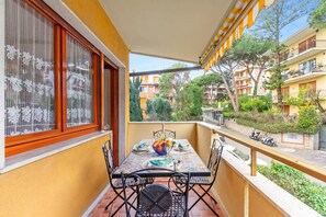 Varanda com mesa posta para refeições, uma cadeira e vista para a rua e edifícios.