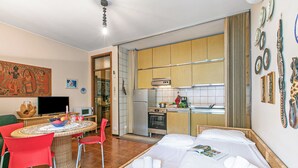 A room with a bed, a dining table with chairs, a kitchen area, and a television. - Sweet Home Silvana - With Terrace & Parking (Sanremo)