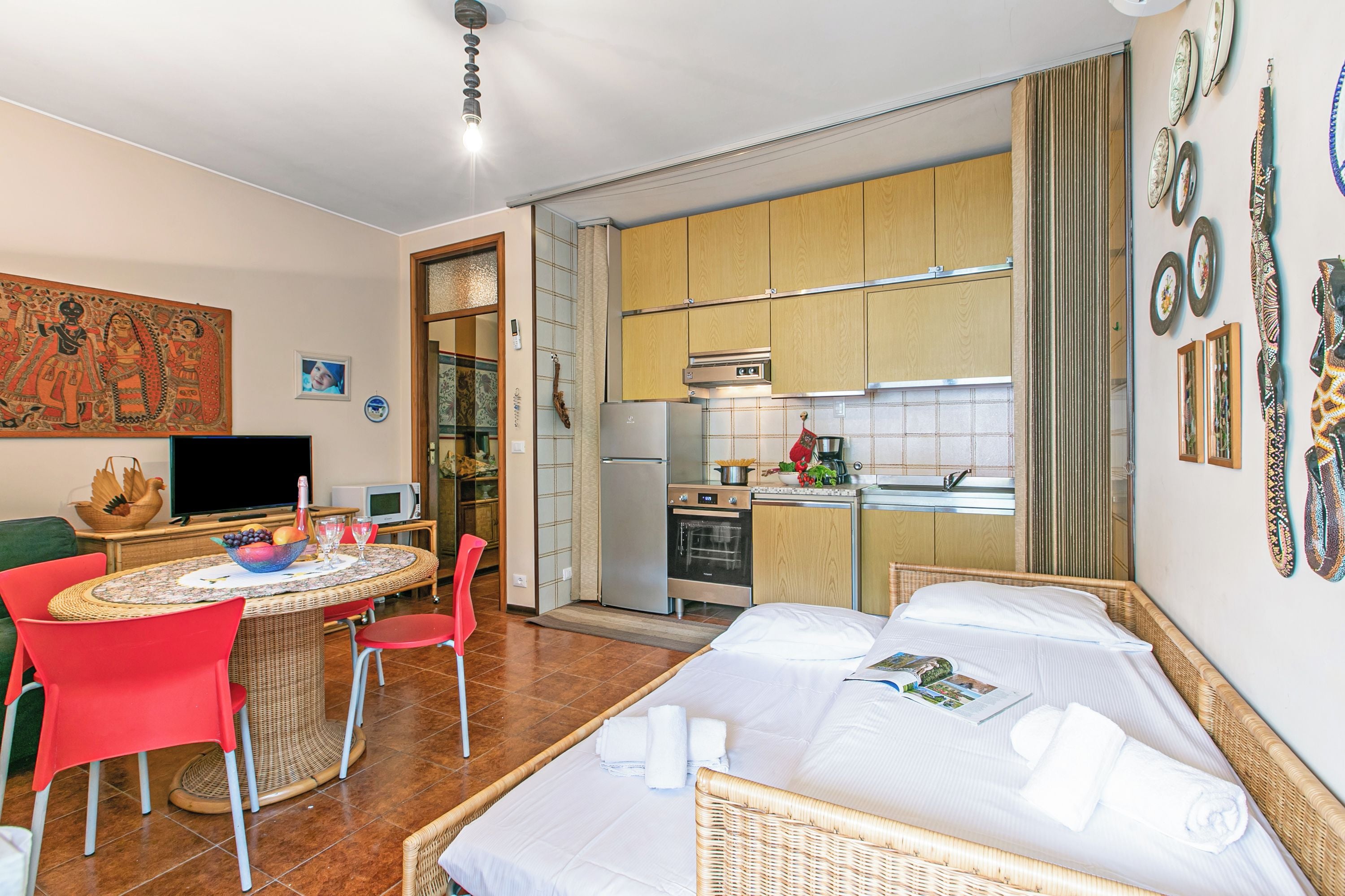 Quarto com cama, mesa de jantar com cadeiras, cozinha e televisão.