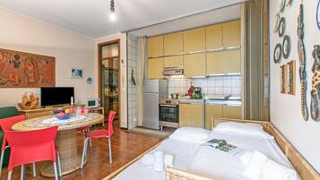Quarto com cama, mesa de jantar com cadeiras, cozinha e televisão.